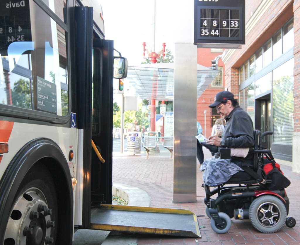 A man in a wheelchair prepared to board a public transit bus.