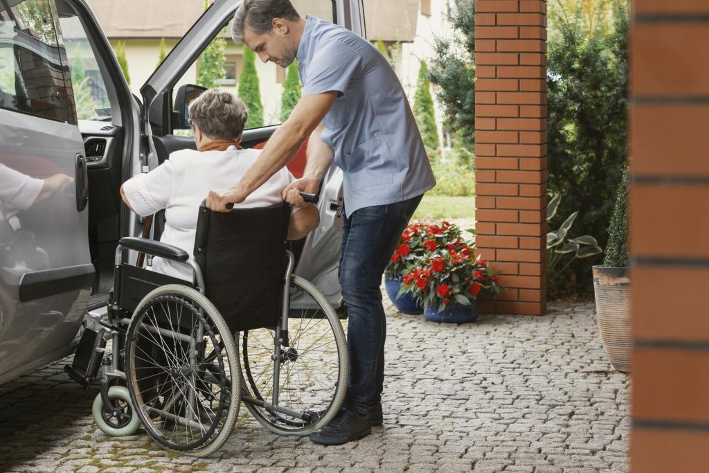 Driver helping senior lady in wheelchair into a car