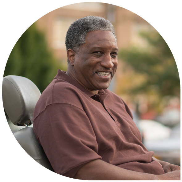 A man who utilizes a wheelchair smiles at the camera as he waits for his non-emergency medical transportation (NEMT) ride to arrive.