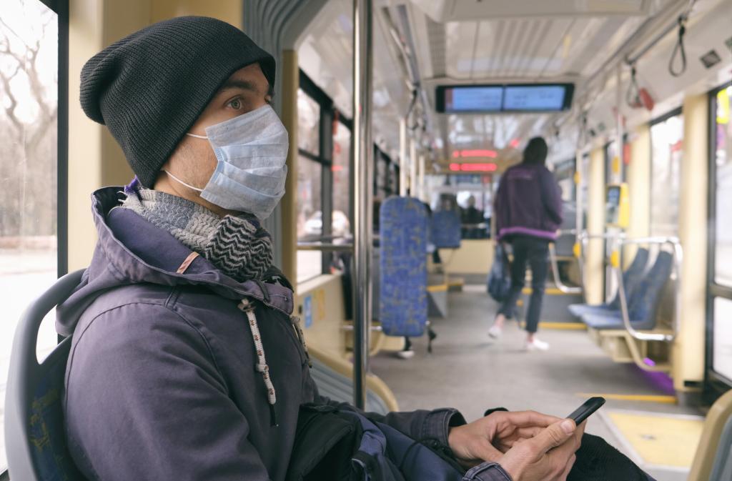 A mean wearing a face mask rides on a public transit train. SDoH like lack of transportation access can negatively affect health outcomes.