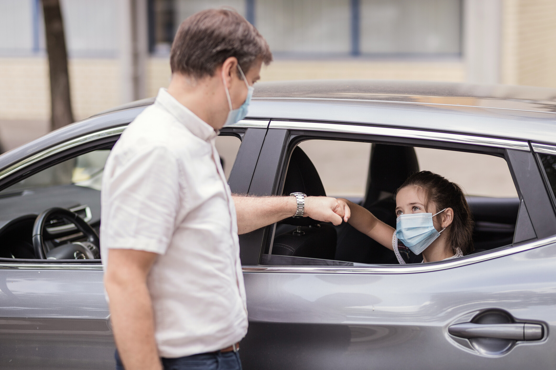 Happy girl with protective mask smiling when greeting with a man standing outside the car