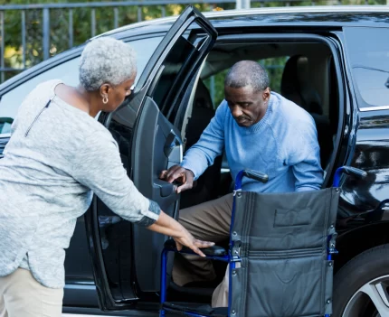 Woman assisting man getting out of a car and into a wheelchair